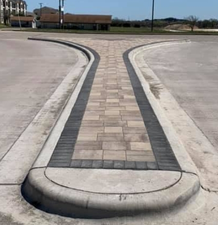 Curved paver median with a banded border and cast concrete curbing dividing a commercial entrance drive