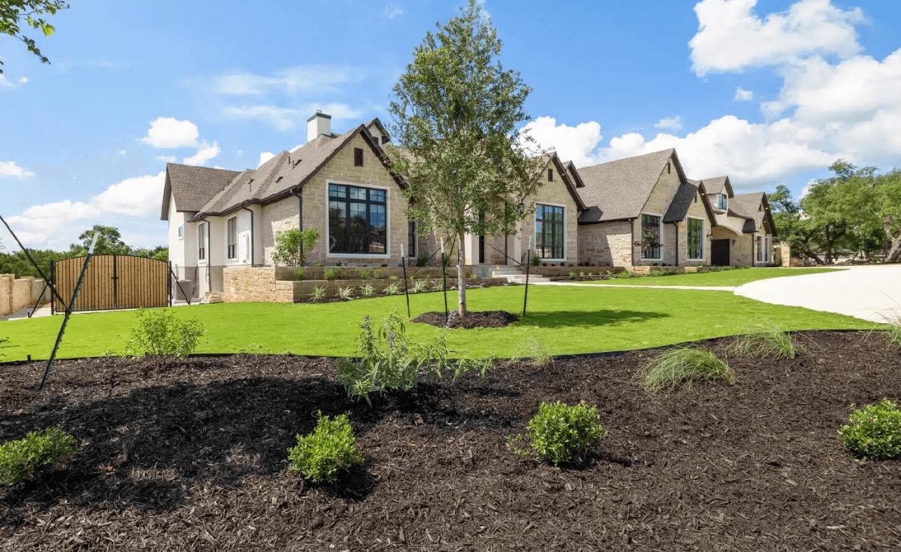 Large stone Hill Country home with fresh sod laid to the drive and newly planted mulch beds across the foreground
